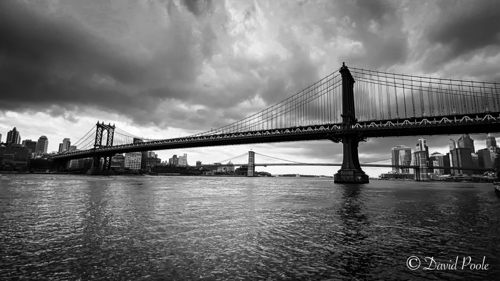 Black and white photo of the Brooklyn Bridge and Manhattan Bridge in New York City, with detailed suspension cables and skyline in the background
