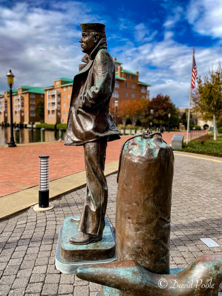 Side view of the Lone Sailor statue in Norfolk, Virginia, showing the sailor’s profile and sea bag with the waterfront in the background