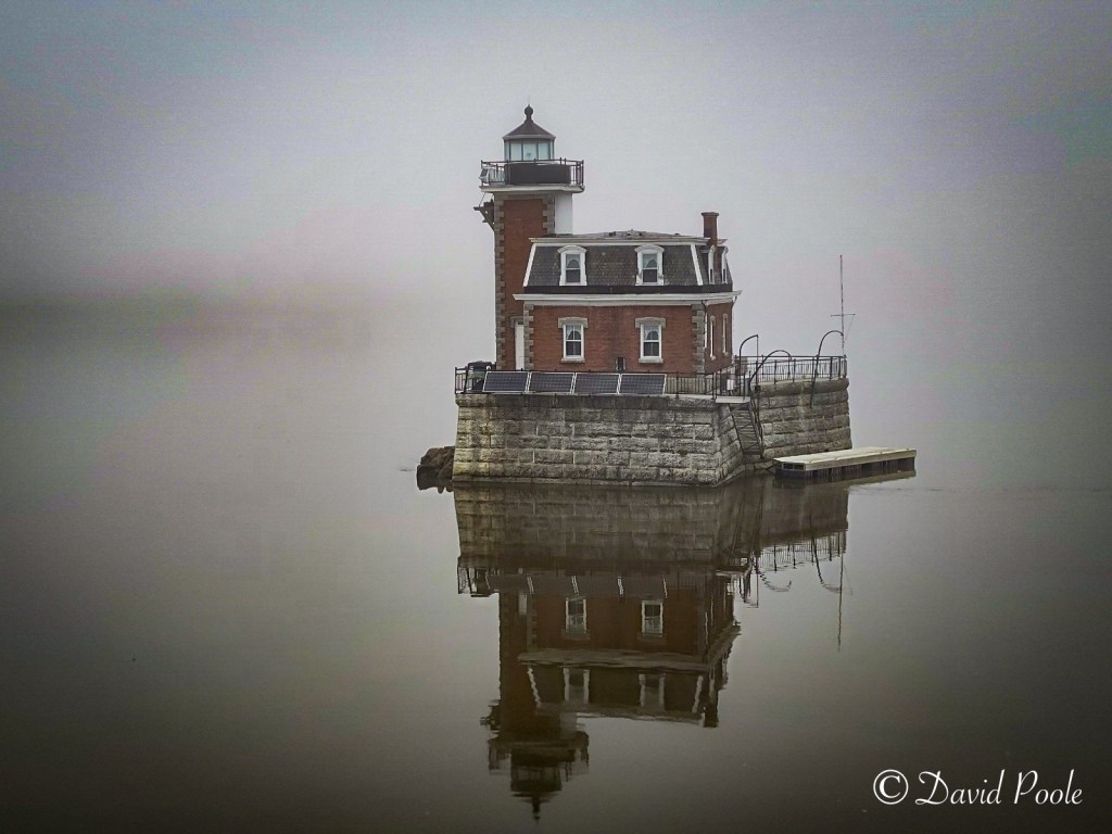 Foggy morning photo of the Hudson River Lighthouse, partially obscured by mist with calm water and a moody atmosphere